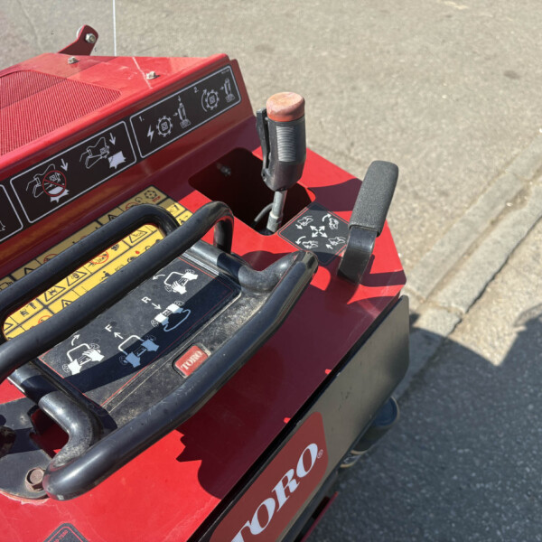 Close-up of a red Toro machine control panel with instructional icons and a black hand guard rail in the foreground.