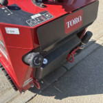 Close-up of a red Toro industrial machine showing the fuel cap, control panel decals, and a black front cover panel on a concrete surface