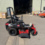 Toro 2000 HDX riding mower in the foreground outside a large workshop, with a wide open entrance and assorted equipment visible inside and to the right