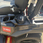 Rear portion of a Toro 2000 HDX riding mower showing a black seat, latch, and rugged frame with a large tire nearby.