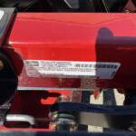 Close-up of a red Toro outdoor equipment frame with an emissions information sticker (EPA standards text) visible on the surface