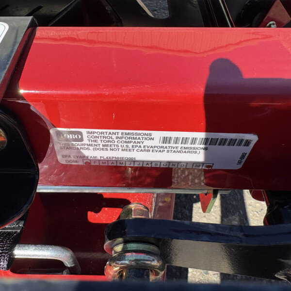 Close-up of a red Toro outdoor equipment frame with an emissions information sticker (EPA standards text) visible on the surface