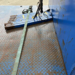 Blue diamond-plate loading deck with rusted ends and a green strap laid across it