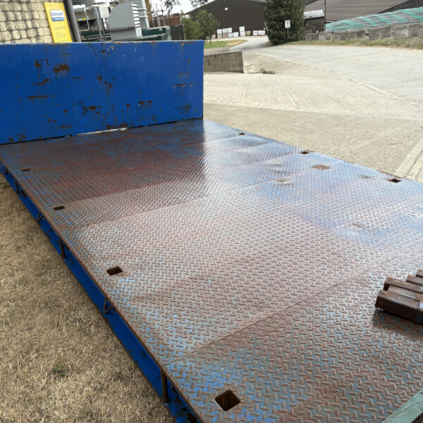 Blue rusted industrial loading ramp with a diamond-plate surface extending toward a paved area.