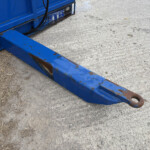 Close-up of blue rusty metal beam and machinery on a dirt/gravel surface.