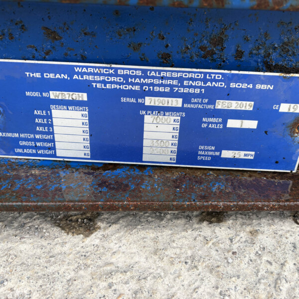 Blue metal identification plate on a rusted surface displaying model and serial numbers.