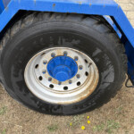 Close-up of a large tractor tire with a blue rim and blue metal frame, showing rust and dirt on the wheel.