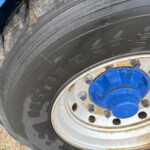 Close-up of a large tractor tire with blue wheel hub and rusty rim, on dry ground.