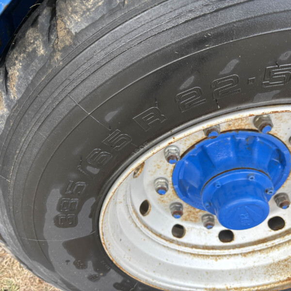 Close-up of a large tractor tire with blue wheel hub and rusty rim, on dry ground.