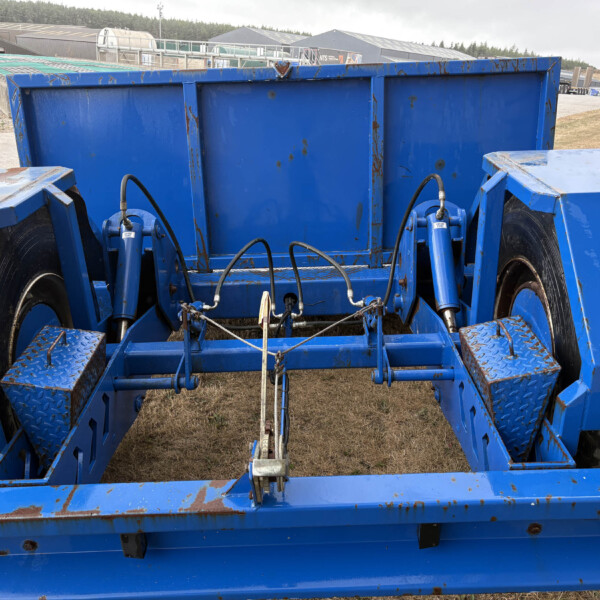 Blue industrial trailer from the inside, showing hydraulic hoses and mechanisms at a construction yard.