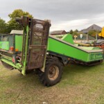 Green Reekie baler on a grassy area with large belt rollers at the front, near a fence.