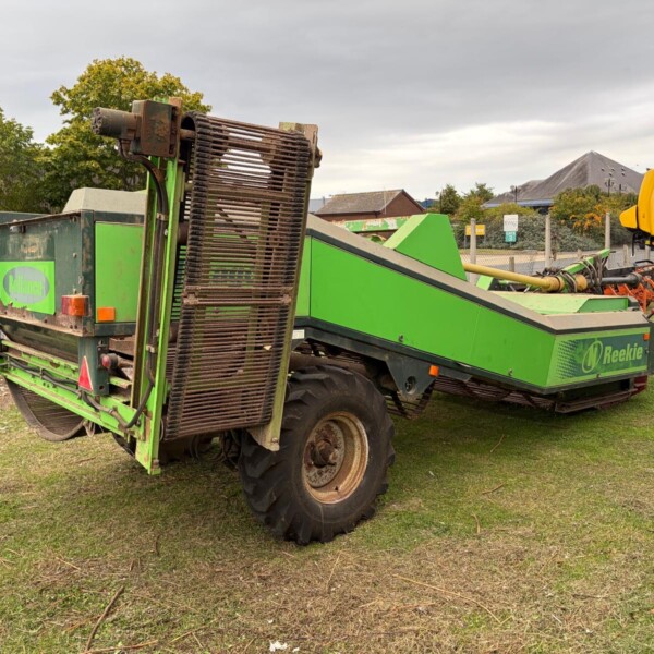Green Reekie baler on a grassy area with large belt rollers at the front, near a fence.