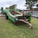 Large green farm implement with a long tow bar lying on grass near a fence, appears idle in a yard.