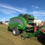 Green McHale Fusion baler attached to a tractor on a grassy farm field under a blue sky with scattered clouds.