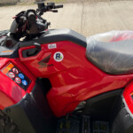 Red Honda ATV with a wrapped plastic seat, handlebars, and control panel visible outdoors.