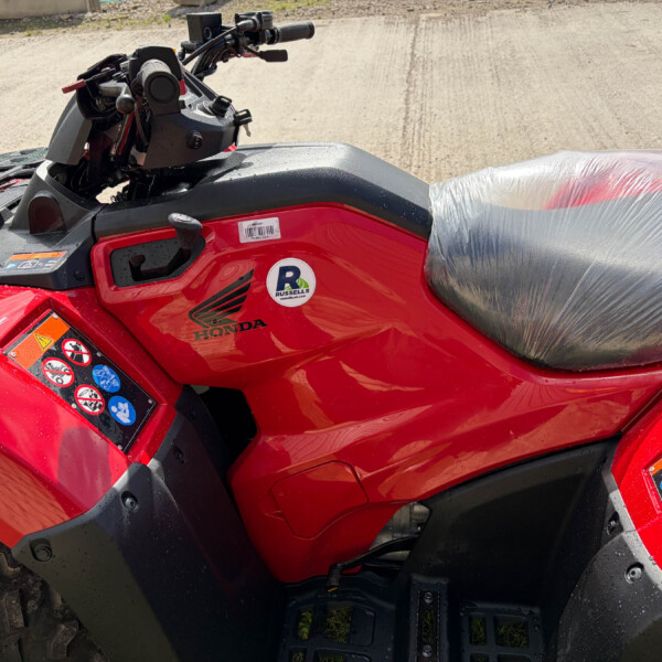 Red Honda ATV with a wrapped plastic seat, handlebars, and control panel visible outdoors.