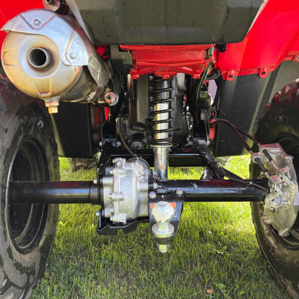Underside of a red off-road vehicle showing large tires, suspension, and exhaust on grass.