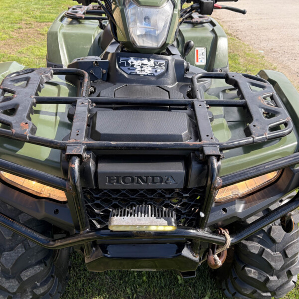 Front view of a green Honda ATV with a metal cargo rack, headlights, and muddy tires on grass.