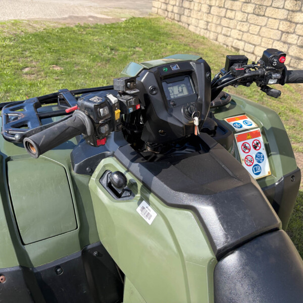 Close-up view of a green ATV handlebar cluster with digital display, switches, and ignition key