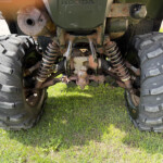 Underside of a rugged off-road vehicle with large knobby tires, exposed suspension, and rusted metal components.
