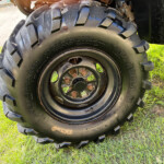 Close-up of a large off-road tire with deep treads mounted on a steel rim, sitting on grass.