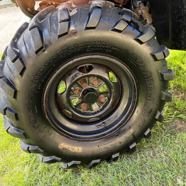 Close-up of a large off-road tire with deep treads mounted on a steel rim, sitting on grass.
