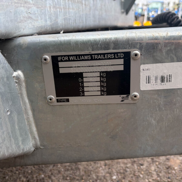 Close-up of a weathered silver trailer showing an identification plate with 'IFOR WILLIAMS TRAILERS LTD' and a barcode, mounted on the side of the trailer.