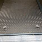 Diamond-pattern metal floor of a trailer with scattered dried leaves along the edges and rails nearby, industrial setting.