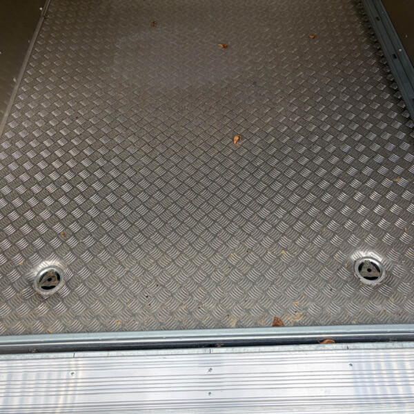 Diamond-pattern metal floor of a trailer with scattered dried leaves along the edges and rails nearby, industrial setting.