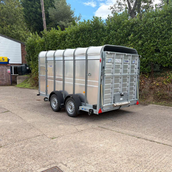 Silver enclosed utility trailer parked in a lot beside a white building with a yellow 'RUSSELLS' sign on the storefront.