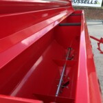 Close-up of glossy red farm equipment with angled side panels; a red circular gear and gray framework visible in the background.