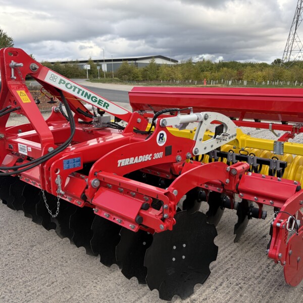 Red Pöttinger Terradisc 3001 soil cultivator with large black discs and hydraulic hoses in a farmyard setting