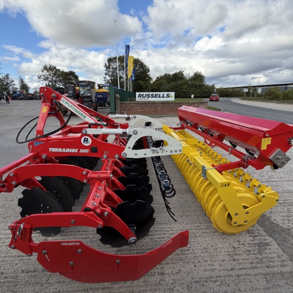 Red Pöttinger Terradisc 3001 farming implement with a yellow seed roller in a dealership yard.