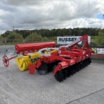 Red TerraDisc 3001 farming implement with yellow discs, parked in an outdoor lot near a green fence and trees in the background.