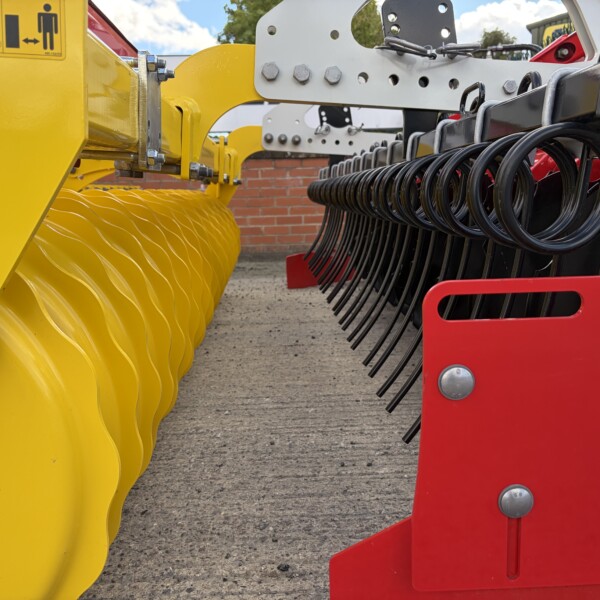 Close-up of a yellow farming header with serrated blades and black tines, mounted to a red frame on the right.