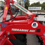Close-up of a red Terradisc 3001 agricultural implement with hydraulic hoses and bolts, at an outdoor equipment yard.