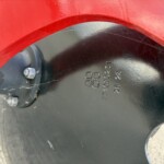Close-up of a red curved fender over a black panel with bolts and stamped numbers visible nearby.