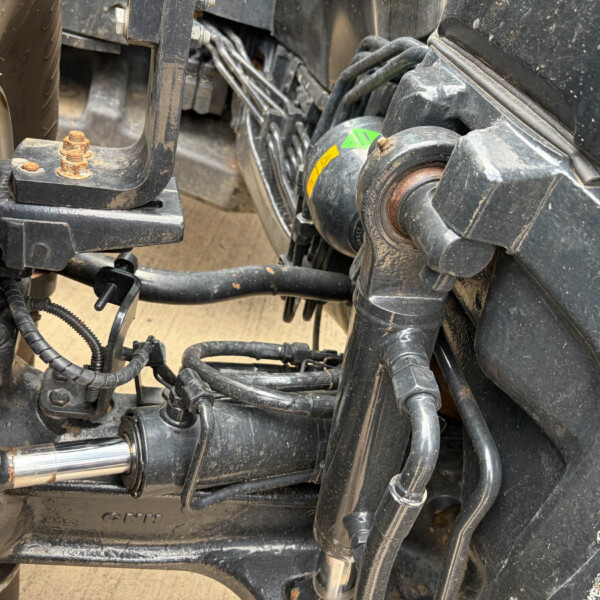 Close-up of a dirt-splattered motorcycle frame showing suspension linkage, wires, and rusted bolts.