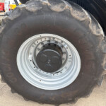 Close-up of a large tractor tire with a silver rim and dusty, worn tread marks on the rubber.