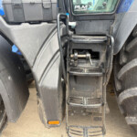Rear view of a heavy vehicle showing steps, ladder, toolbox, and large rugged tires between the axles.