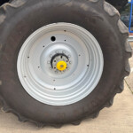 Close-up of a large muddy tractor tire with a light gray rim and yellow hub, parked on a concrete surface near a storefront window.