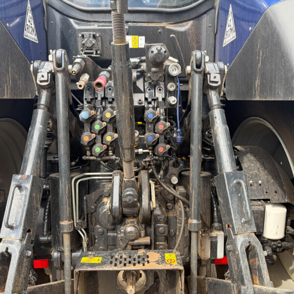 Rear hydraulic control panel on a tractor, with colored knobs, hoses, and linkage arms (dusty from use).