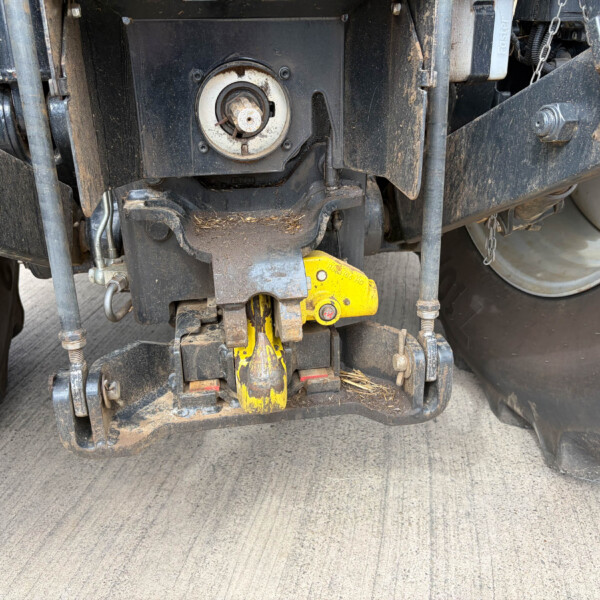 Close-up of a dirty trailer hitch and mechanical components under a trailer, featuring a yellow hitch/lock pin and mounting bolts.