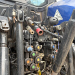 Close-up of a hydraulic control manifold on a tractor, with colored caps and fittings framing a dusty, mechanical panel.