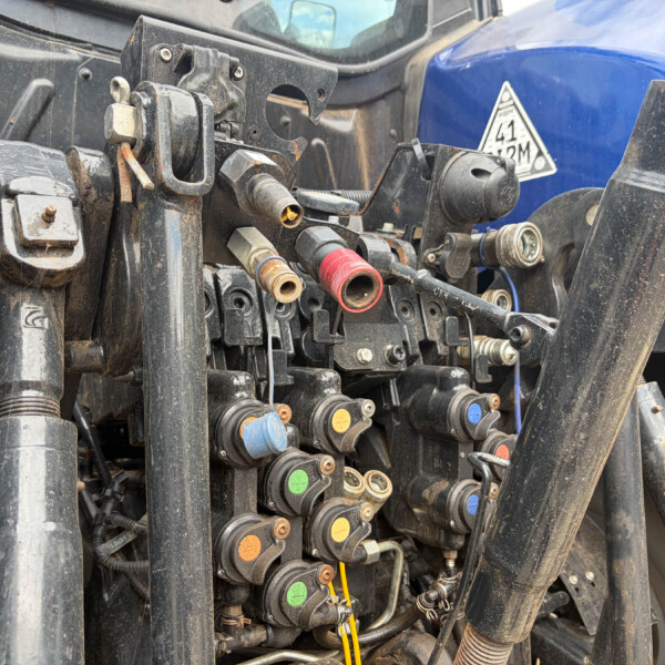 Close-up of a hydraulic control manifold on a tractor, with colored caps and fittings framing a dusty, mechanical panel.