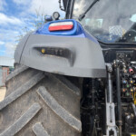 Close-up of a blue construction vehicle with large treaded tire, exposed hydraulic controls, and a cabin window in the background.