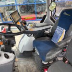 Bus driver's cockpit with steering wheel, mounted tablet, and complex control panel next to a blue driver’s seat.