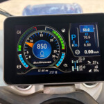 Close-up of a car's digital instrument cluster: circular tachometer showing 850, green/yellow/red indicators, and a parked (P) indicator with fuel and other readouts on the right side.