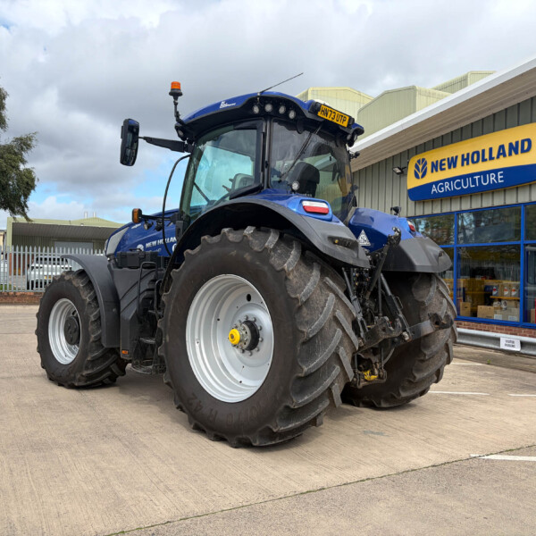 Blue New Holland tractor parked outside an agriculture store with a bright yellow and blue sign behind it.