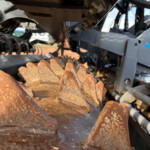 Close-up of rusted, jagged steel teeth from industrial machinery, with a gray metal frame in the background.